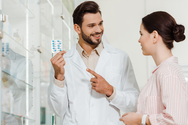 Farmacista sorridente che punta al blister con pillole per il cliente in farmacia
 - Foto, immagini