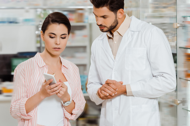 Žena zákazník ukazuje drogista smartphone podle lékárny vitríny - Fotografie, Obrázek