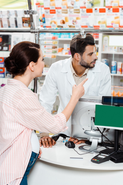 Cliente embarazada señalando medicamentos a farmacéutico en farmacia
 - Foto, Imagen