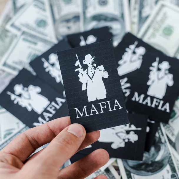 KYIV, UKRAINE - NOVEMBER 22, 2019: cropped view of man holding playing card with mafia letters near cash  - Valokuva, kuva