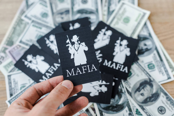 KYIV, UKRAINE - NOVEMBER 22, 2019: cropped view of man holding playing card with mafia letters near cash on table  - Foto, imagen