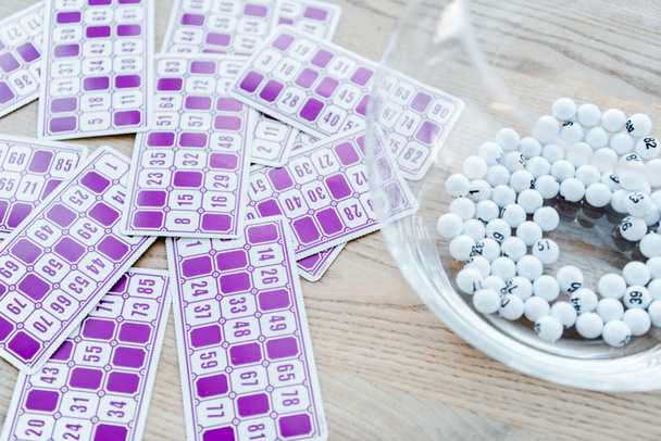 фиолетовые лотерейные билеты с номерами возле чаши с шариками
  - Фото, изображение