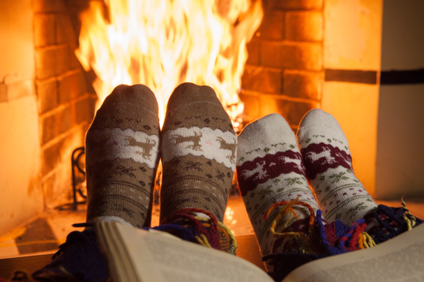 Чоловік і жінка в теплих в'язаних шкарпетках з чашками гарячого удару перед каміном
 - Фото, зображення