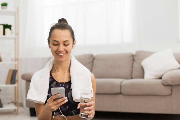 Smiling girl with water and phone after exercising at home - Foto, Imagen