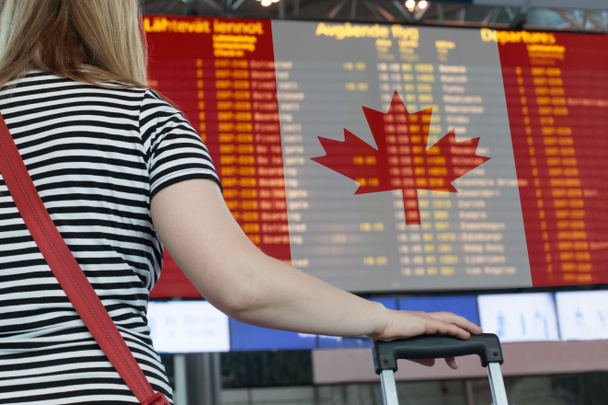 Μια γυναίκα κοιτάζει τον πίνακα αποτελεσμάτων στο αεροδρόμιο. Επιλέξτε μια χώρα του Καναδά για ταξίδια ή μετανάστευση. - Φωτογραφία, εικόνα