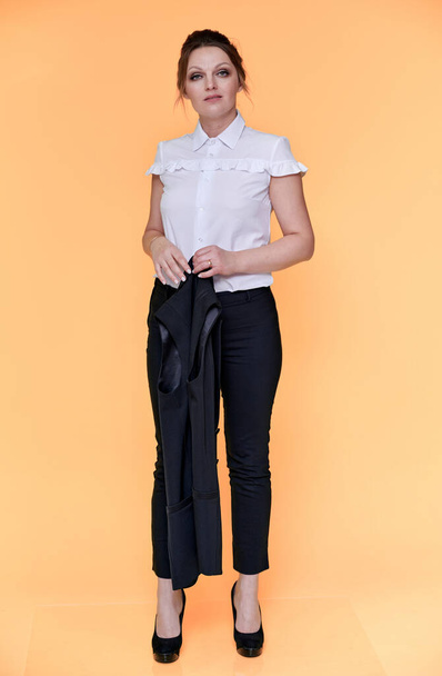 Business concept. Full-length portrait of an adult pretty woman of 40 years old with good makeup in a business suit on a yellow background. Standing right in front of the camera with a smile. - Foto, afbeelding