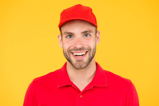 man delivery service in red tshirt and cap. friendly shop assistant. food order deliveryman. cashier vacancy. Fast and free parcel delivery. happy guy. dealer yellow wall. Salesman cashier career - Valokuva, kuva