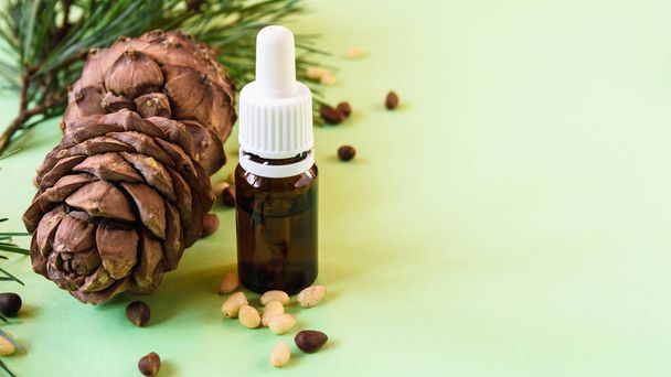 koncept přírodní kosmetiky, borové šišky s ořechy a láhev oleje na zeleném pozadí - Fotografie, Obrázek