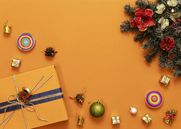 明るいオレンジの背景にマルチカラーのクリスマスのおもちゃ、枝の緑の木、青いリボン、トップビュー、中央のコピースペースとオレンジの箱の贈り物 - 写真・画像