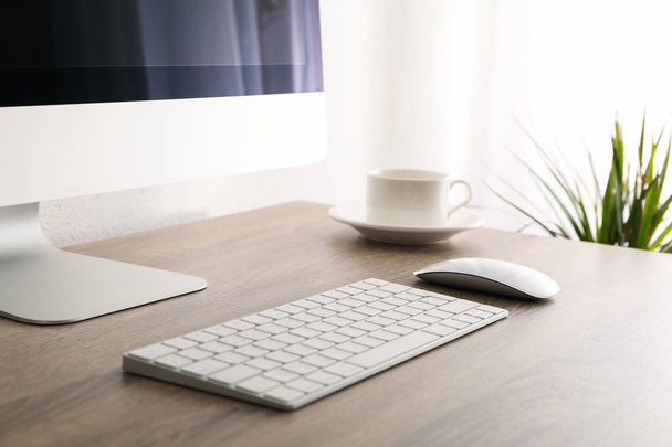 Lugar de trabajo con ordenador, taza con platillo sobre mesa de madera y pla
 - Foto, Imagen