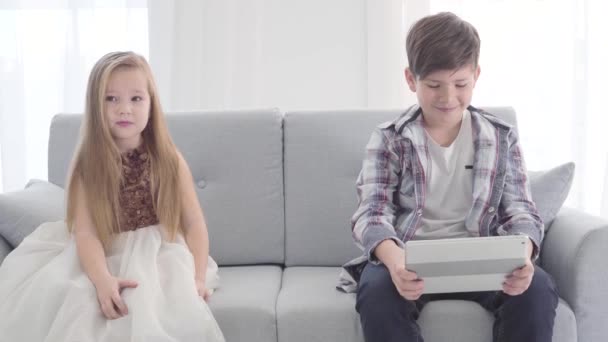 Portrait of Caucasian little boy looking at tablet screen, cute girl sitting next to him throwing shy glance at her love. Childhood, first love. - Séquence, vidéo