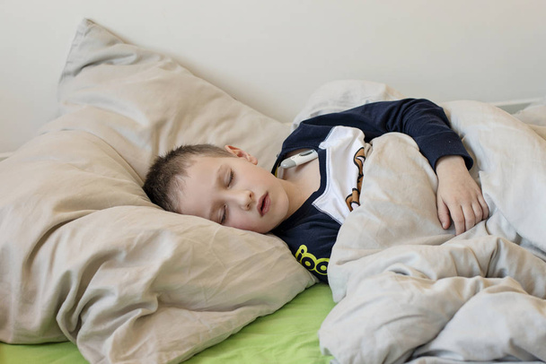 Menino doente pré-escolar com os olhos fechados deitado na cama com um termômetro digital
 - Foto, Imagem