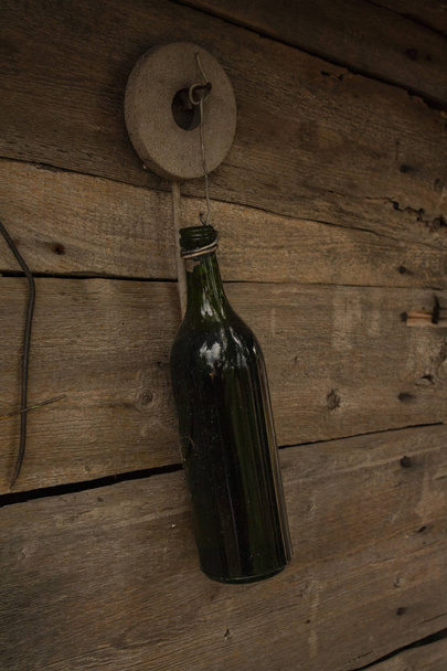 dark green bottle on a background of wooden boards. empty glass bottle. wire hanging bottle - Photo, Image