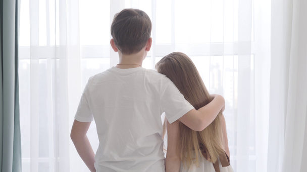 Camera moving away from Caucasian girl and boy standing together in front of the window. Girls head is on boys shoulder. First love, happiness. - Felvétel, videó