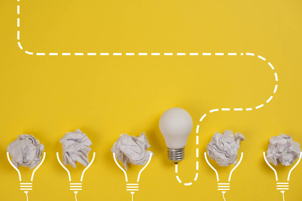 new idea concept with crumpled office paper and white light bulb on yellow background. Creative solution during brainstorming session concept. Flat lay, top view, copy space - Zdjęcie, obraz