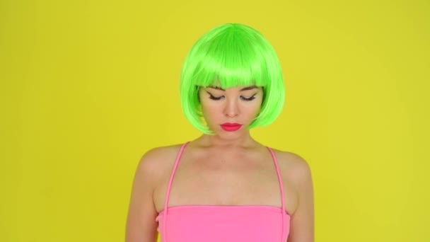 Beautiful woman in a green short wig and pink bikini posing on a yellow background. Portrait of a girl with sensual red lips. - Materiał filmowy, wideo