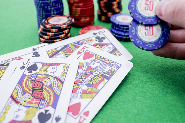 Hand mit zwei blauen Pokerchips neben einem Stapel Chips und einigen Karten - Foto, Bild