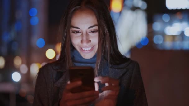 Closeup of prety smiling woman using smartphone walking at night city - Felvétel, videó