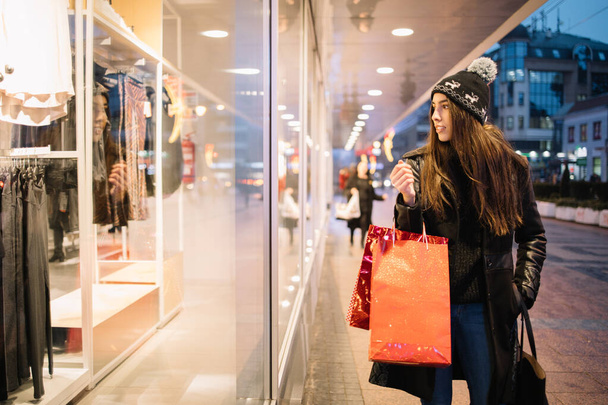 Dziewczyna stojąca przed sklepem i patrząca na ubrania - Zdjęcie, obraz