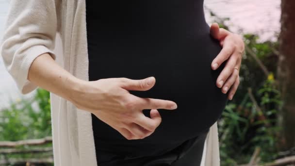 Primer plano de las manos de la mujer embarazada tocando suavemente su barriga
 - Metraje, vídeo