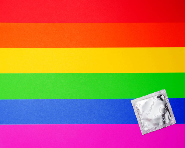 Condoom op de achtergrond van de regenboog vlag. Beschermd en veilig seksconcept. Vlakke lay, bovenaanzicht. Kopieerruimte - Foto, afbeelding