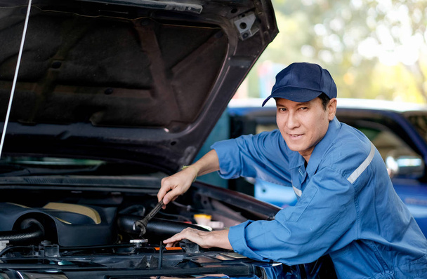Close up of Asian automotive mechanic with blue uniform check the car in the area of hood and engine in the garage. - 写真・画像