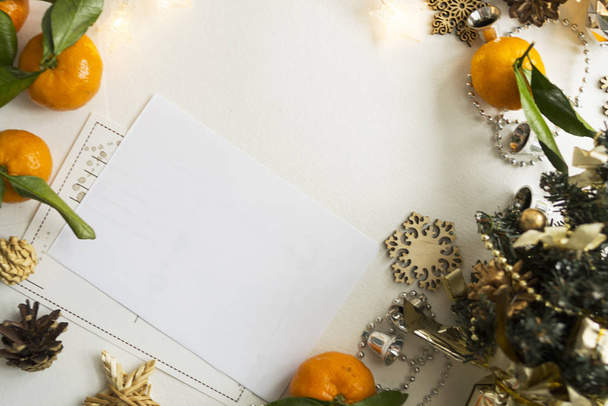 White sheet, postcard lies on the table. Around the layout of citrus fruits, snowflakes, garlands and lights. The concept of a holiday and celebration. - Фото, изображение