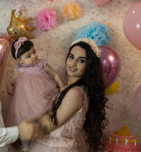 Mama met een dochtertje. Het kind viert een verjaardag. Tegen de achtergrond van roze ballen. Mama 's liefde voor de baby. Een meisje met mooie zwarte ogen. - Foto, afbeelding