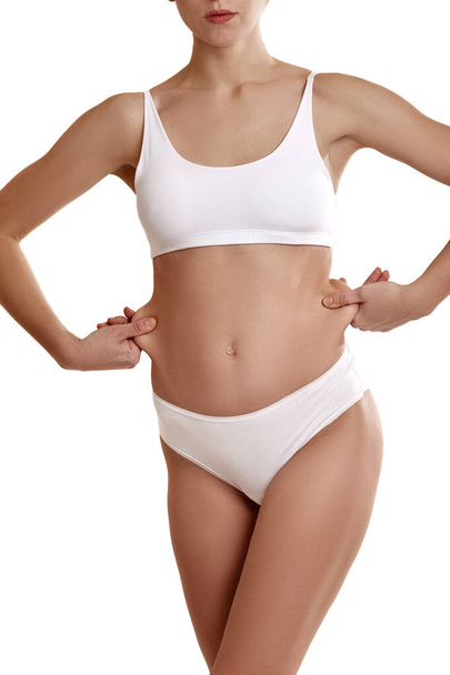 Perfect, slim, young body of a girl in white underwear. Weight loss and healthy eating. Girl showing fat on her belly. The problem of obesity. Plastic surgery. - Zdjęcie, obraz
