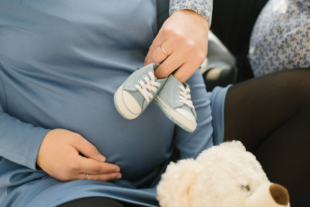 Botines azules del futuro bebé en manos del padre en el vientre de una mujer embarazada. Esperando un bebé
 - Foto, imagen
