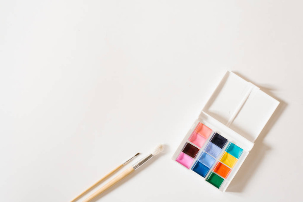 Pitture ad acquerello di diversi colori in fossi in una scatola bianca e pennelli con manici in legno su sfondo bianco. Ricevuto. Corsi di disegno e master per la scuola d'arte
 - Foto, immagini