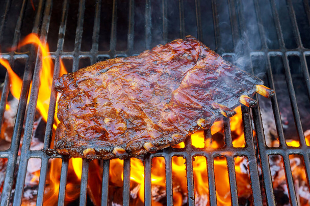 Grilled pork ribs cooking on charcoal with flame. - Photo, Image