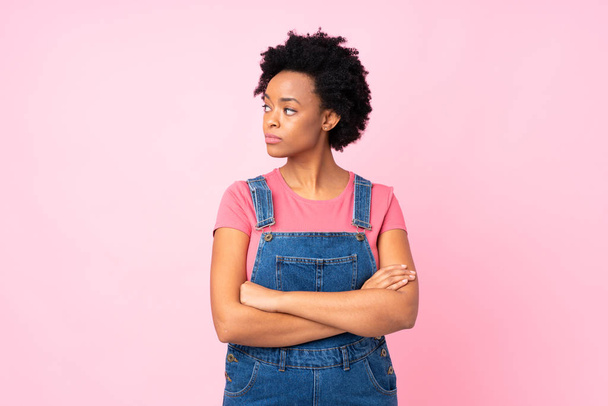 African american woman with overalls over isolated pink background looking side - Фото, изображение