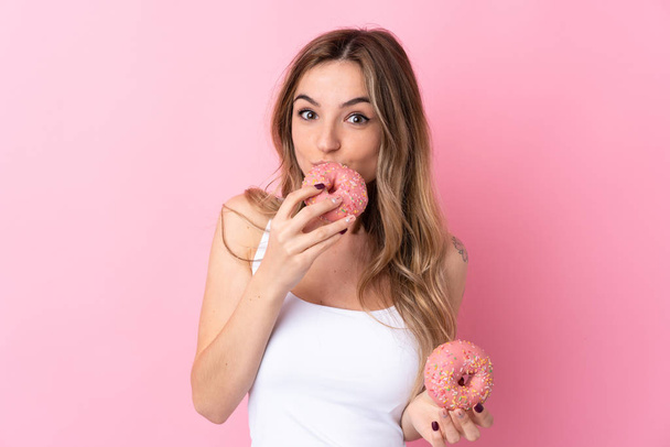 Молодая женщина на изолированном розовом фоне держит пончик - Фото, изображение