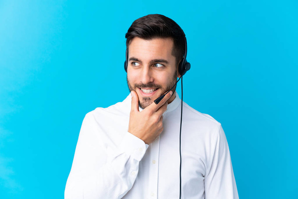 Telemarketer man working with a headset over isolated blue background thinking an idea - Photo, Image