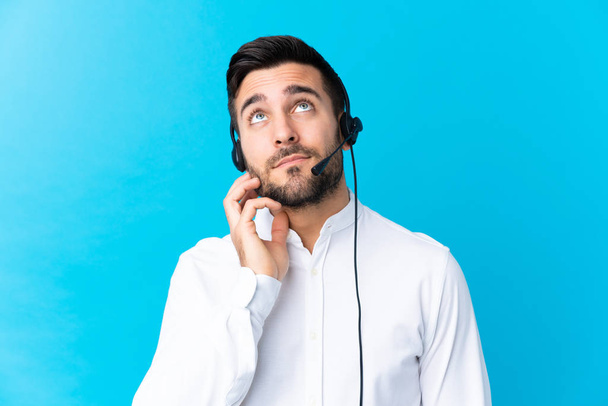 Hombre del telemarketer que trabaja con un auricular sobre fondo azul aislado que piensa una idea
 - Foto, imagen