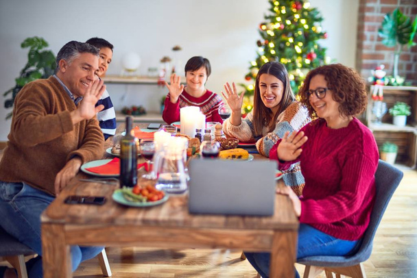 Hermosa familia sonriendo feliz y confiada. Comer pavo asado hacer videocall usando el ordenador portátil celebrando la Navidad en casa
 - Foto, imagen