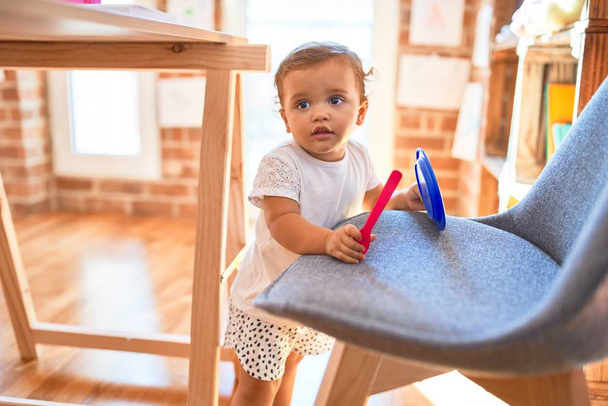 Красивый ребенок играет с пластиковой посудой и столовыми приборами вокруг много игрушек в детском саду
 - Фото, изображение