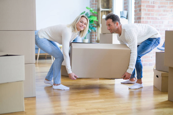 Young beautiful couple moving cardboard boxes at new home - Zdjęcie, obraz