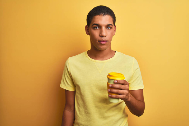 Fiatal jóképű arab férfi ivás elvenni kávé felett elszigetelt sárga háttér magabiztos kifejezés okos arc gondolkodás komoly - Fotó, kép