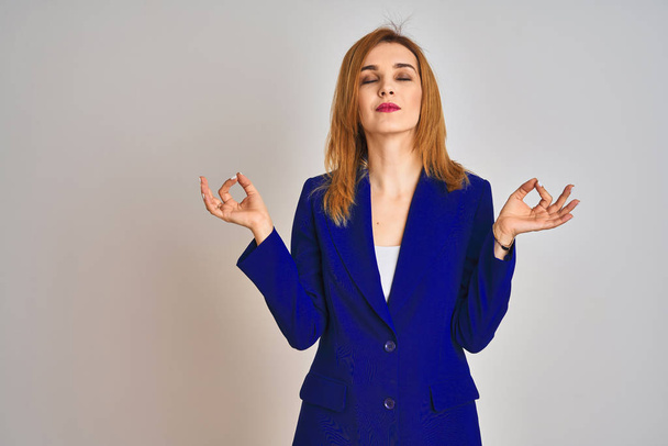 Redhead caucasian business woman wearing a suit over isolated background relax and smiling with eyes closed doing meditation gesture with fingers. Yoga concept. - Фото, зображення