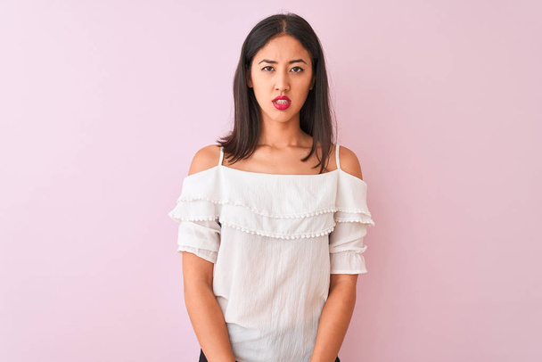 Beautiful chinese woman wearing white t-shirt standing over isolated pink background skeptic and nervous, disapproving expression on face with crossed arms. Negative person. - Foto, Imagen