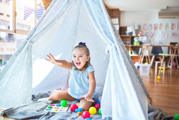 Jeune belle fille blonde enfant appréciant jouer à l'école avec des jouets à la maternelle, souriant heureux de jouer à l'intérieur tente indienne à la maison
 - Photo, image