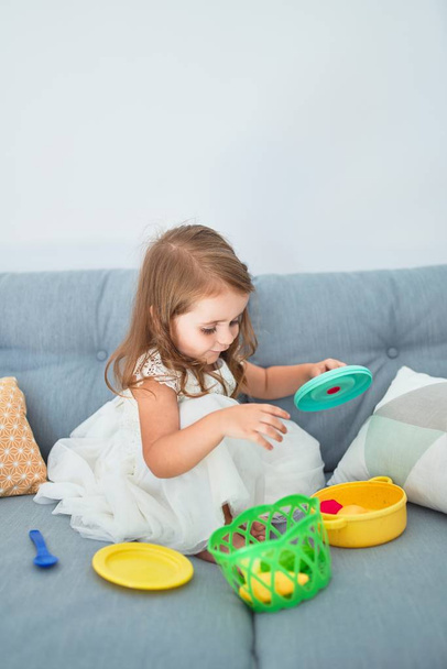 Чарівний блондинка малюк сидить на дивані, готуючи їжу та столові іграшки вдома
 - Фото, зображення