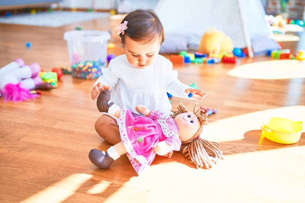 Красива дитина щаслива в дитячому садку навколо барвистих іграшок, які грають з лялькою
 - Фото, зображення