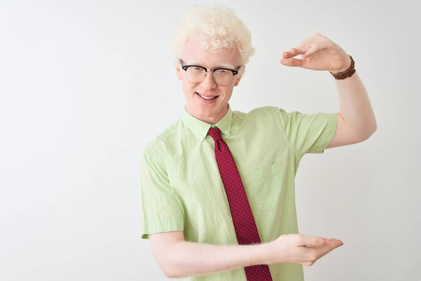 Jonge albino zakenman dragen shirt en stropdas staan over geïsoleerde witte achtergrond gebaren met de handen tonen grote en grote maat teken, maat symbool. Lachend kijkend naar de camera. Meetconcept. - Foto, afbeelding