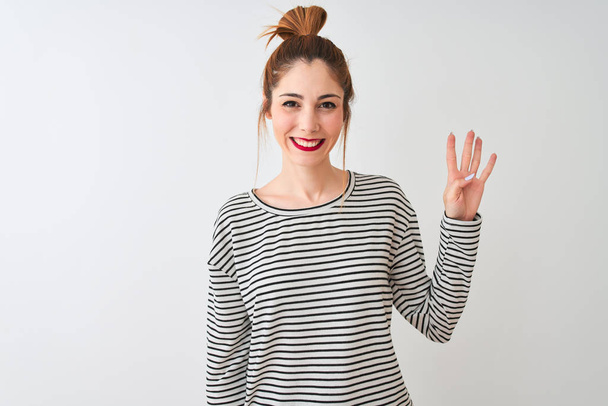 Redhead woman wearing navy striped t-shirt standing over isolated white background showing and pointing up with fingers number four while smiling confident and happy. - Valokuva, kuva
