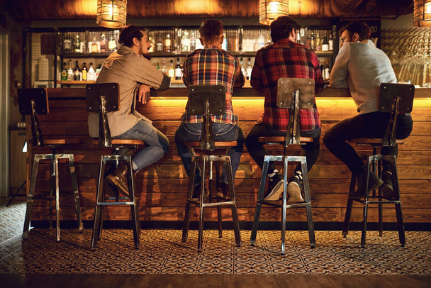 Rear view friends sitting on chairs talking at the bar in a bar. - Zdjęcie, obraz