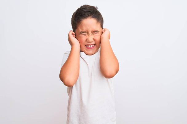 Beautiful kid boy wearing casual t-shirt standing over isolated white background covering ears with fingers with annoyed expression for the noise of loud music. Deaf concept. - Photo, Image