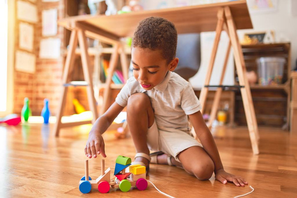 Bellissimo bambino africano americano che gioca con blocchi di legno treno giocattolo intorno a un sacco di giocattoli all'asilo
 - Foto, immagini
